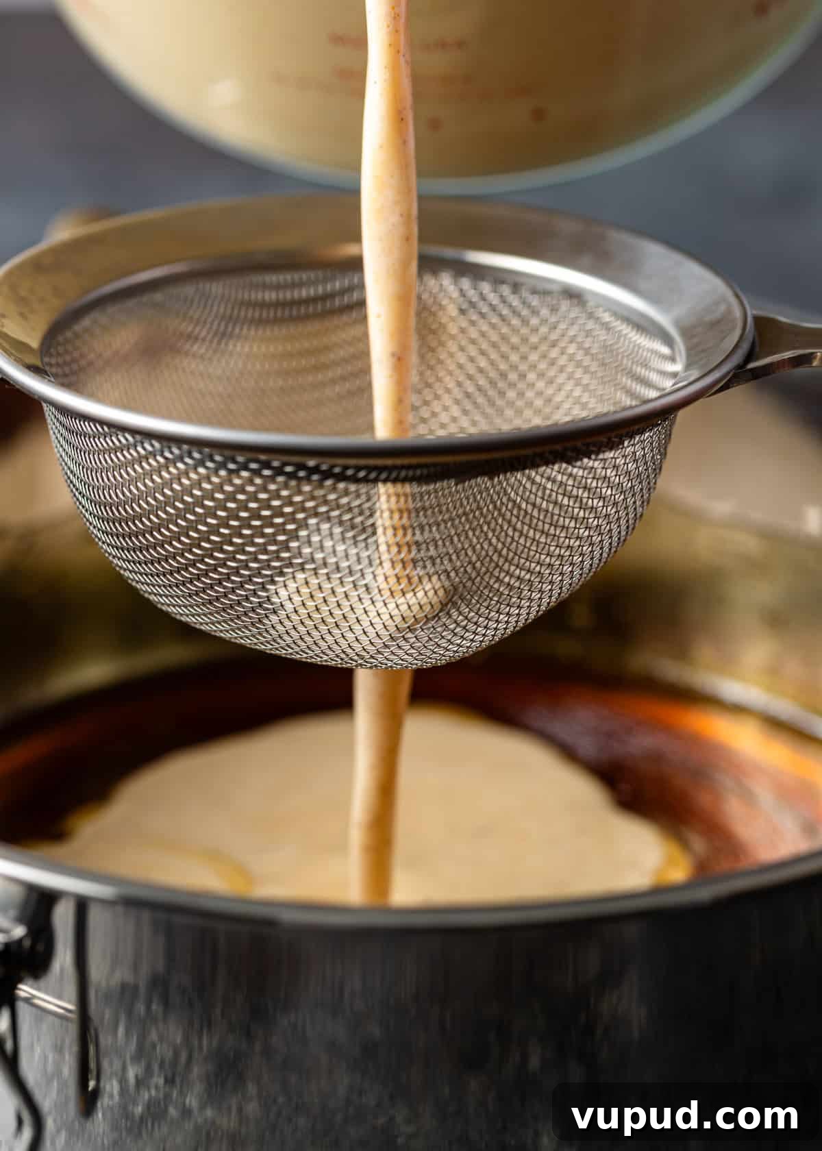 side view process shot: straining the custard on top of the caramel