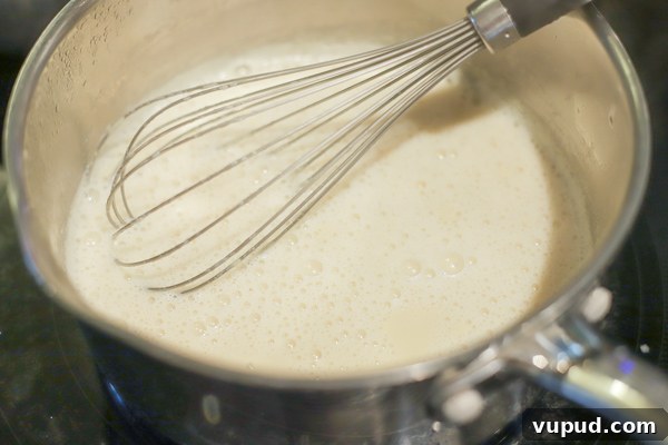 Homemade Sweetened Condensed Milk: Simple Stovetop Recipe 5 simmering milk, cream, and maple syrup in a saucepan with a whisk