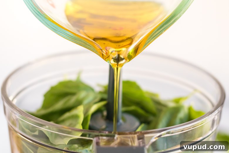 Homemade Nut-Free Pesto Recipe: Flavorful Dairy-Free Sauce 4 Olive oil being poured into a food processor to make nut free basil pesto