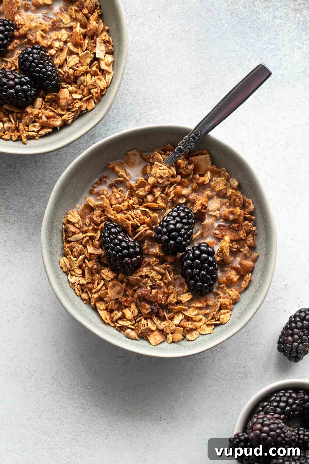 Maple Walnut Granola Recipe: Crunchy Homemade Clusters 2 Overhead view of maple granola in a grey bowl and topped with almond milk and blackberries, with another bowl of granola off to the side.