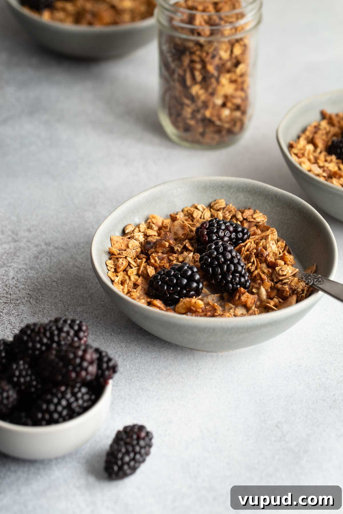 Maple Walnut Granola Recipe: Crunchy Homemade Clusters 7 Side view of a bowl of maple syrup granola topped with blackberries, with granola in the background.