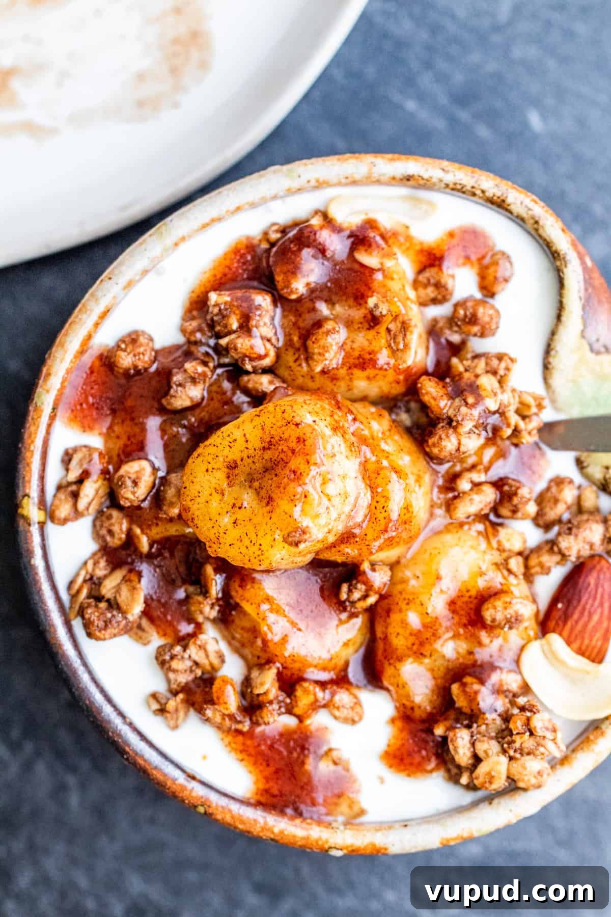 Pan-Fried Cinnamon Bananas with Maple Glaze Recipe 5 Overhead shot of bananas on top of granola and yogurt in small tan bowl.