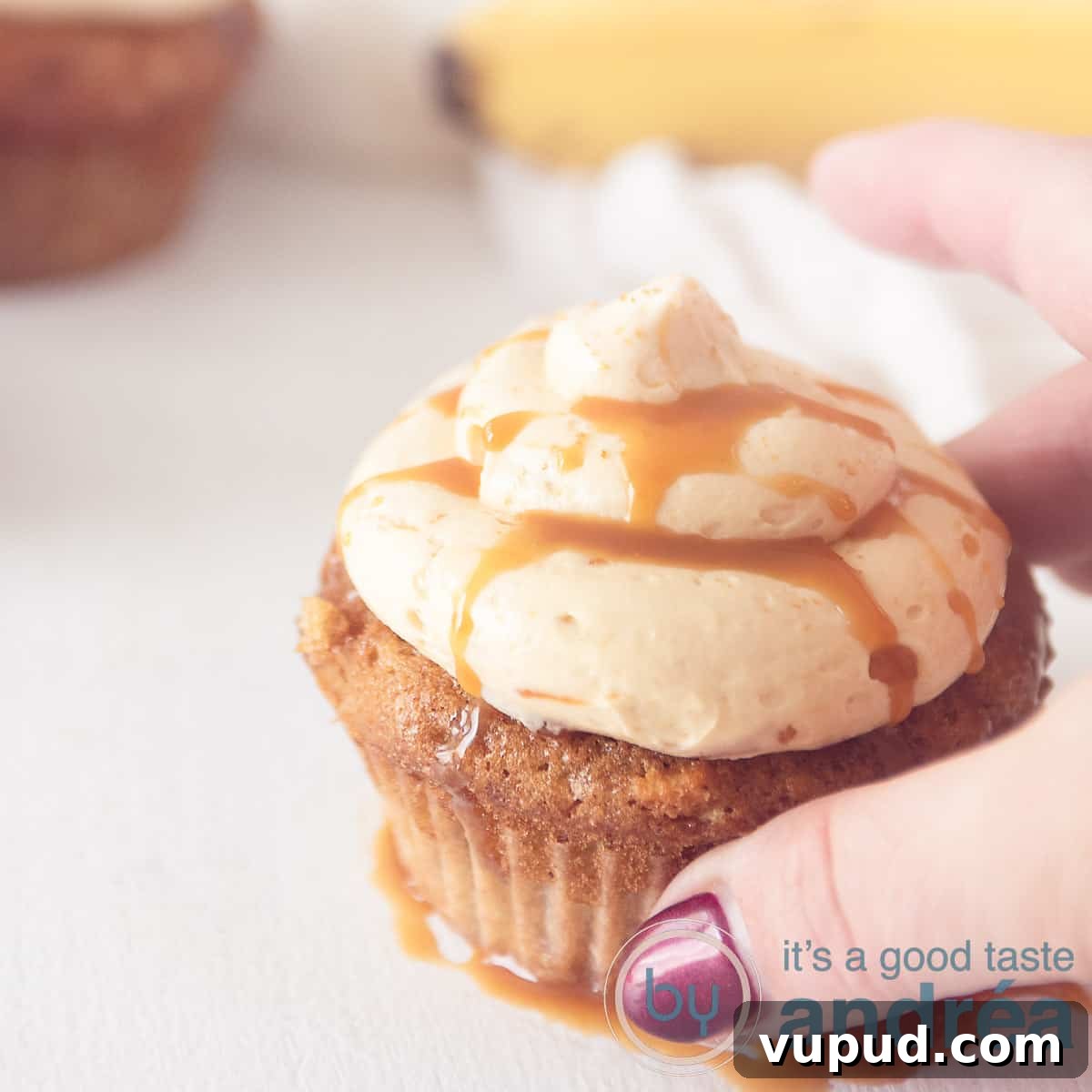 Caramel Banana Cupcakes with Gooey Salted Caramel Drizzle 7 A square photo with a cupcake with caramel cream and caramel sauce. A hand takes the cupcake