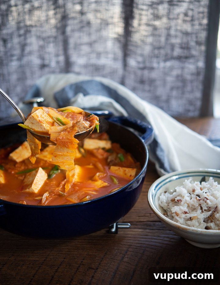 Tomato Kimchi Stew Recipe: Savory Korean Tomato-Kimchi Jjigae 2 A ladle of kimchi tofu stew served with a bowl of rice.