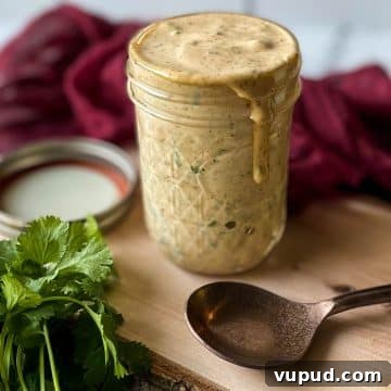 Chipotle sauce in a glass jar sits on a wooden cutting board with a spoon, parsley and a red linen.
