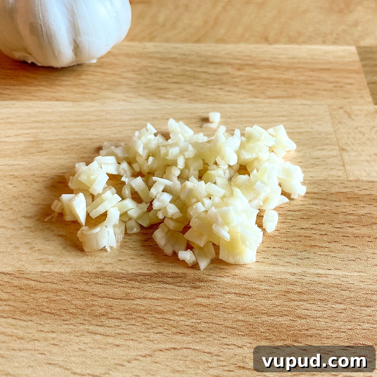 Creamy Cilantro-Lime Crema Recipe for Tacos & Bowls 4 Minced garlic with a head of garlic in the background on a butcher block cutting board