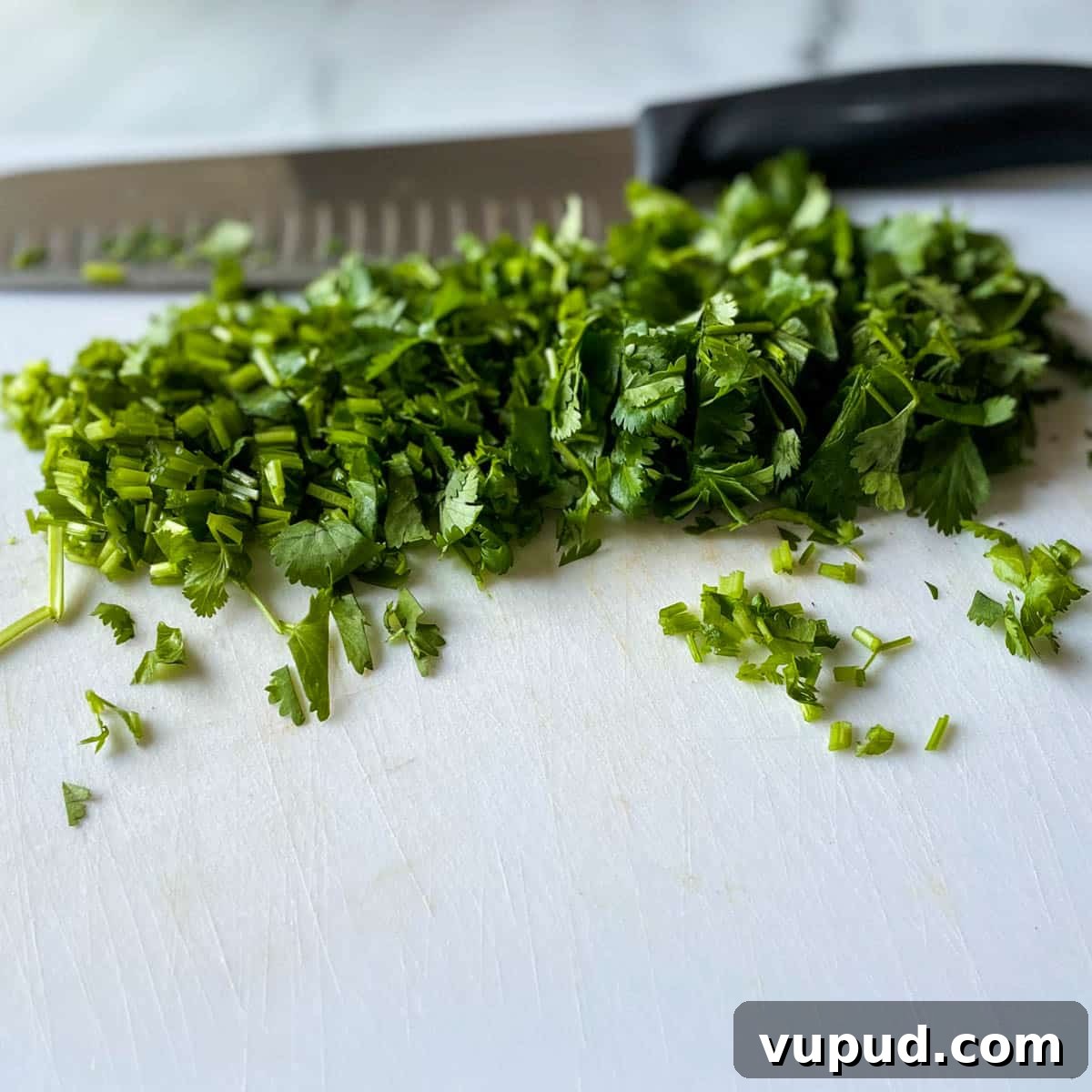 Creamy Cilantro-Lime Crema Recipe for Tacos & Bowls 5 Chopped fresh cilantro is shown on a white cutting board with a kitchen knife in the background.