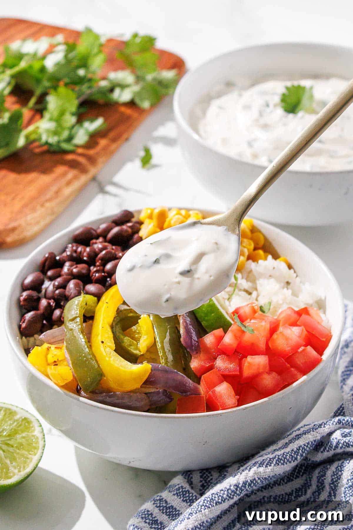 Creamy Cilantro-Lime Crema Recipe for Tacos & Bowls 9 A colorful burrito bowl with a dollop of cilantro lime crema being added from a spoon.