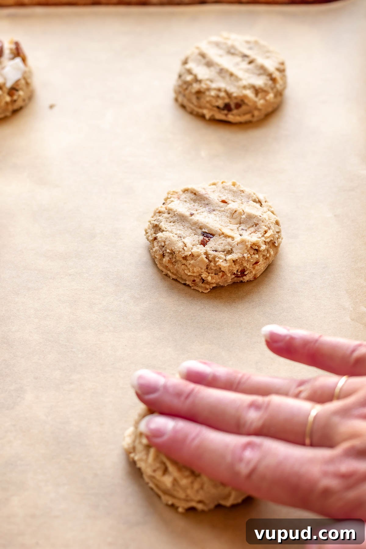 Chewy Coconut Pecan Cookies Recipe for Crispy Edges and Gooey Center 11 A hand gently flattens cookie dough on a sheet pan.