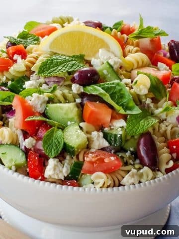 Greek Pasta salad in a white bowl with lemon wedge on top.