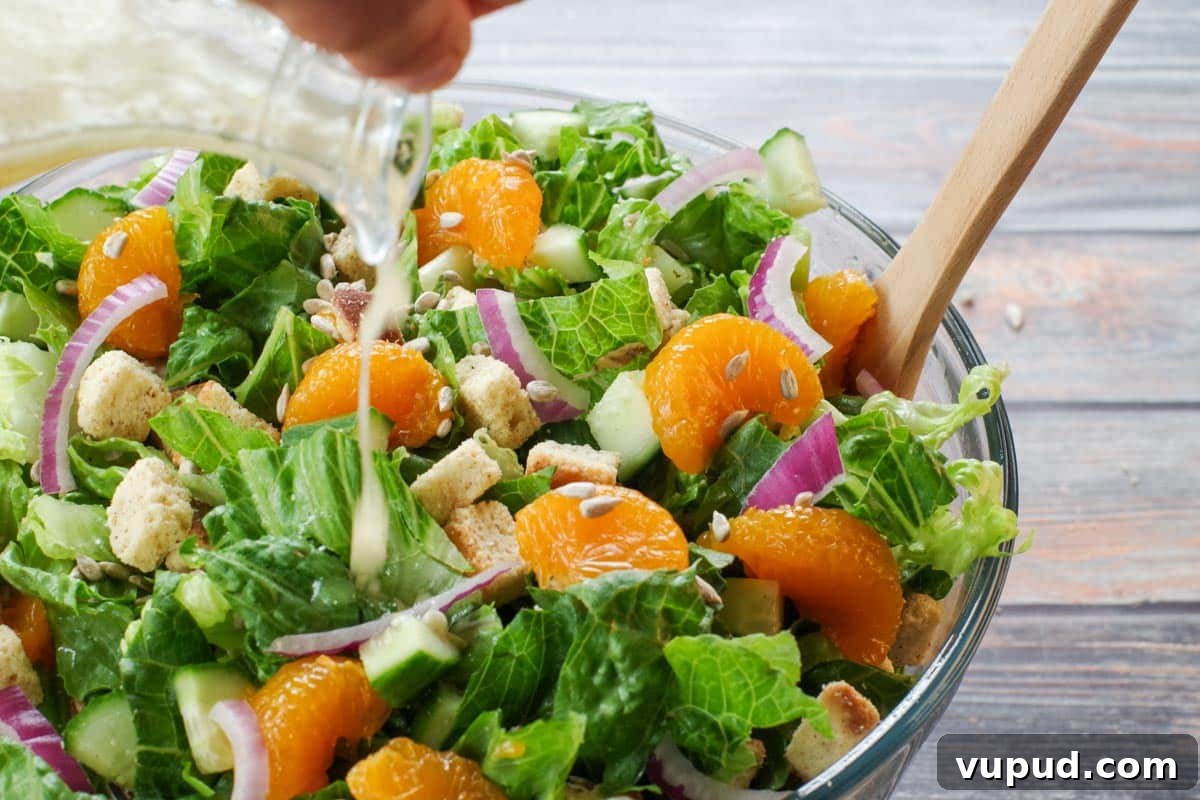 Zesty Mandarin Orange Salad Recipe with Citrus Vinaigrette 7 mandarin orange salad in a large glass bowl with dressing being poured on it from a glass container