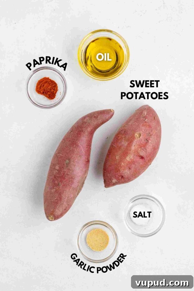 Crispy Fried Sweet Potatoes with Honey-Citrus Glaze 3 Two whole sweet potatoes are surrounded by small bowls of oil, paprika, salt, and garlic powder, each labeled with text naming the ingredient. The items are arranged on a white background.