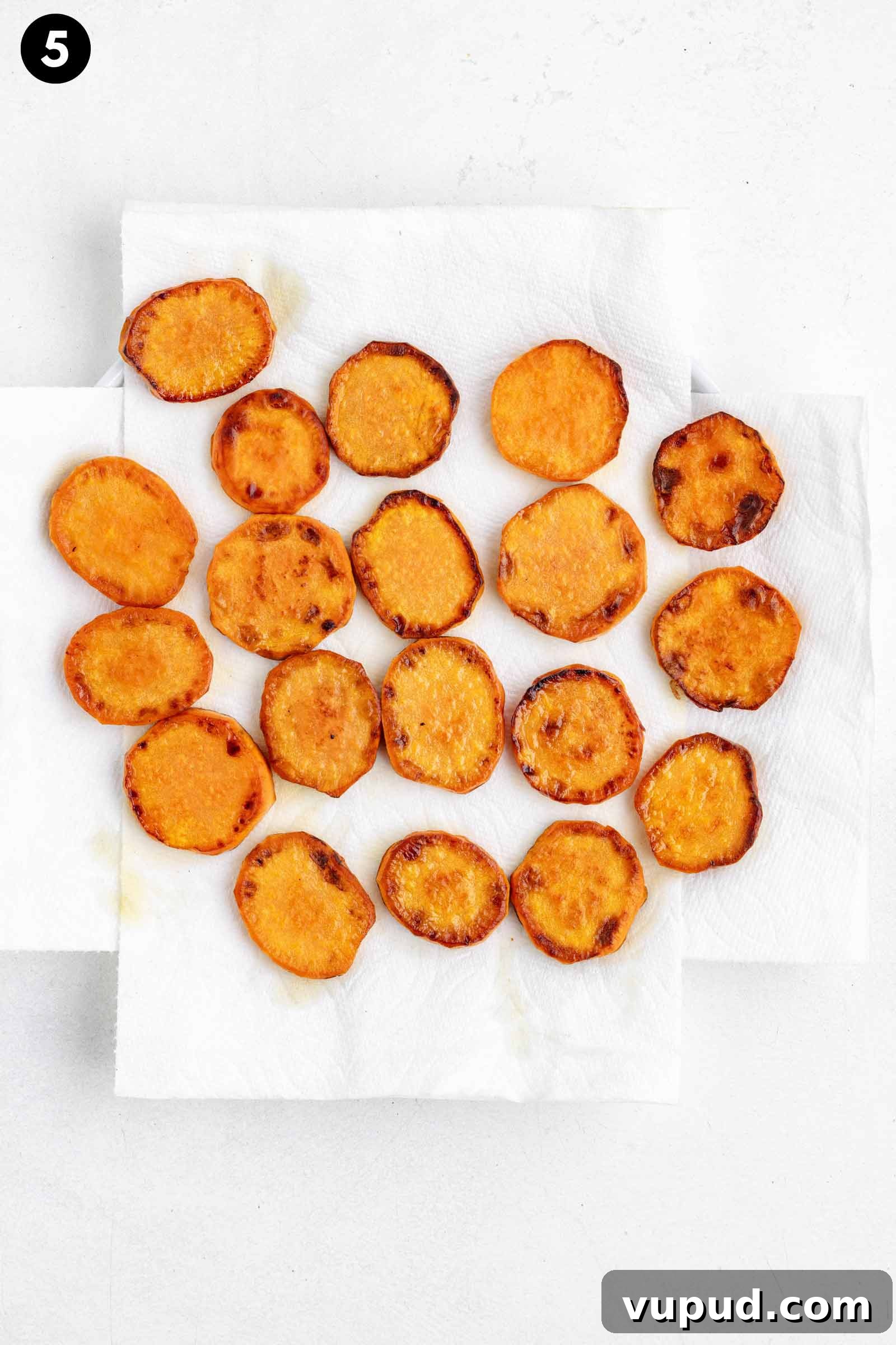 Crispy Fried Sweet Potatoes with Honey-Citrus Glaze 5 fried sweet potatoes are arranged in a single layer on two overlapping white paper towels, displayed on a light-colored surface.