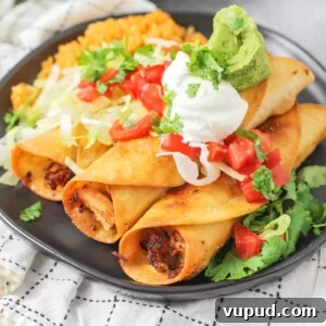 Chicken flautas rolled up and topped with guac, sour cream and more on black plate.