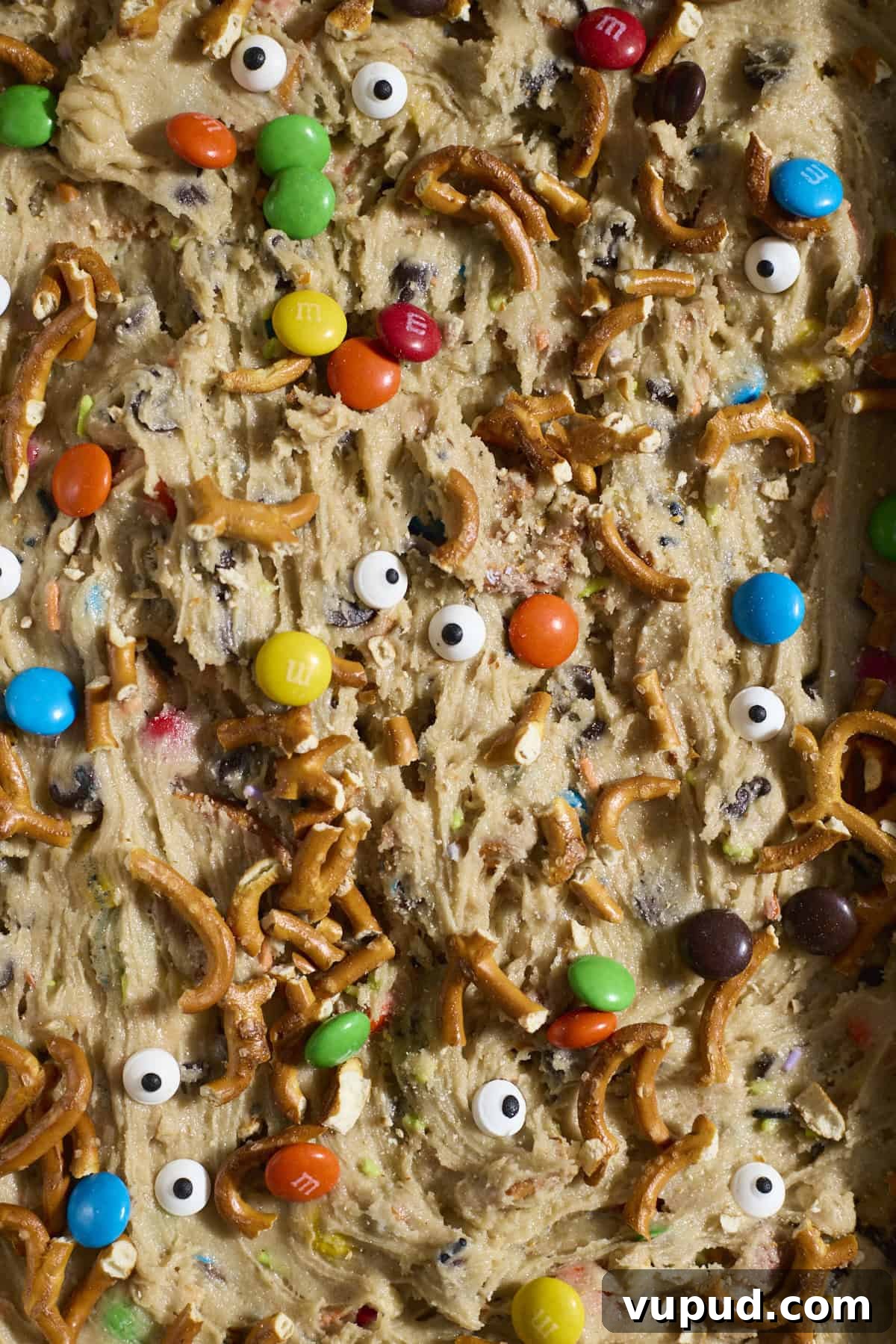 Halloween Sourdough Discard Kitchen Sink Cookie Bars 8 Pretzels, M&Ms and googly eyes on top of the cookie batter.
