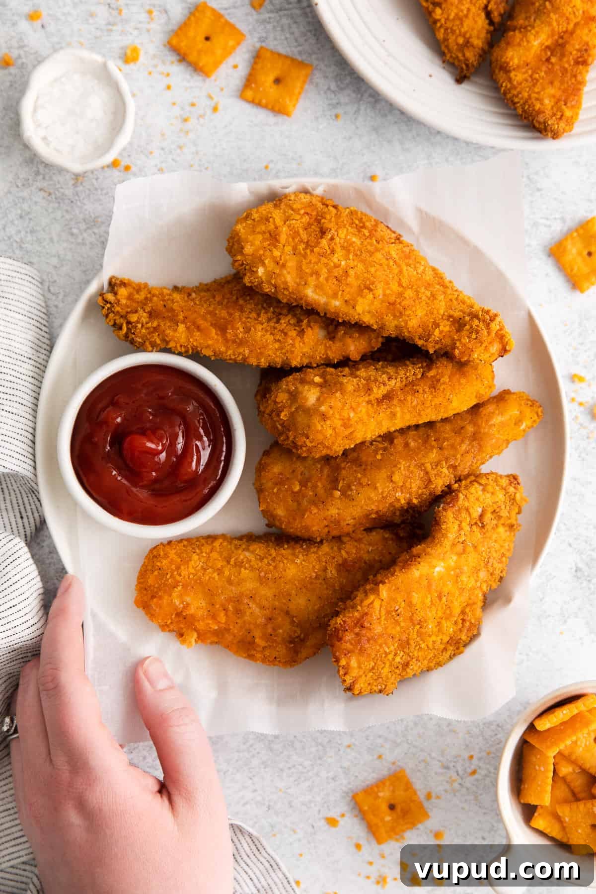 These easy Cheez-It breaded chicken fingers take one of your favorite snacks and turn it into a crispy, cheesy chicken masterpiece! Made in the air fryer in minutes. Chicken fingers on a plate with ketchup.