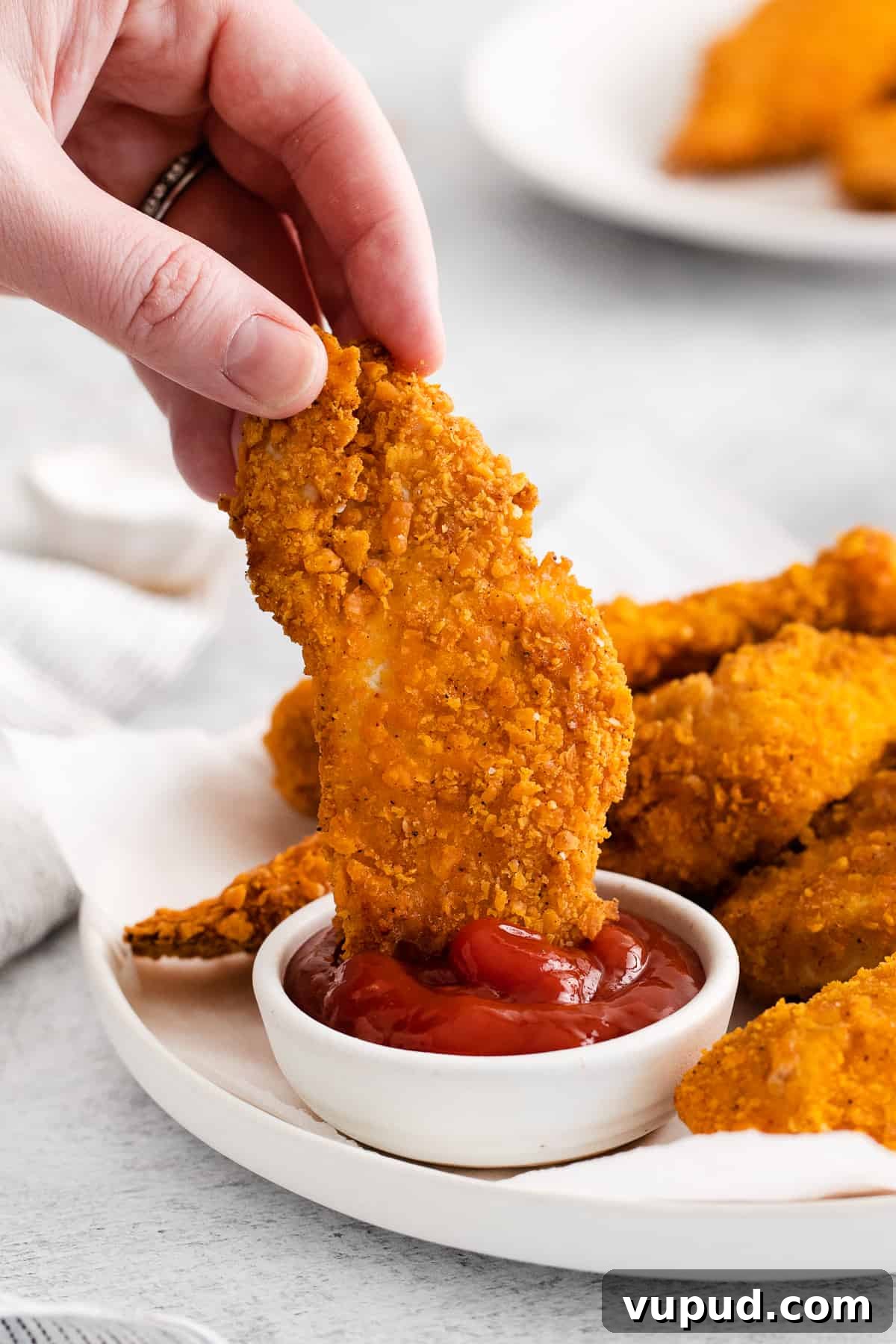 These easy Cheez-It breaded chicken fingers take one of your favorite snacks and turn it into a crispy, cheesy chicken masterpiece! Made in the air fryer in minutes. Hand dipping a chicken finger in ketchup.