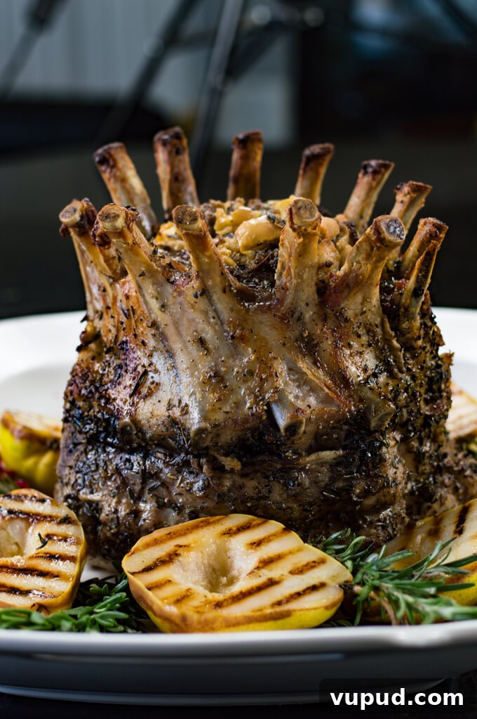 Savory Herb-Crusted Pork Crown Roast Recipe 4 A cooked crown roast of pork sits on a white serving tray with grilled pears and fresh rosemary around the roast.
