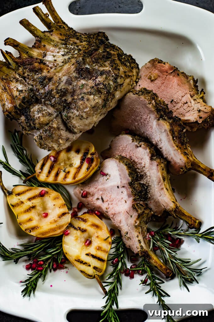 Savory Herb-Crusted Pork Crown Roast Recipe 5 Slices of crown roast of pork sit on a white serving tray. Half of the whole roast sits next to them along with grilled pears, fresh rosemary and some pomegranate seeds sprinkled around.