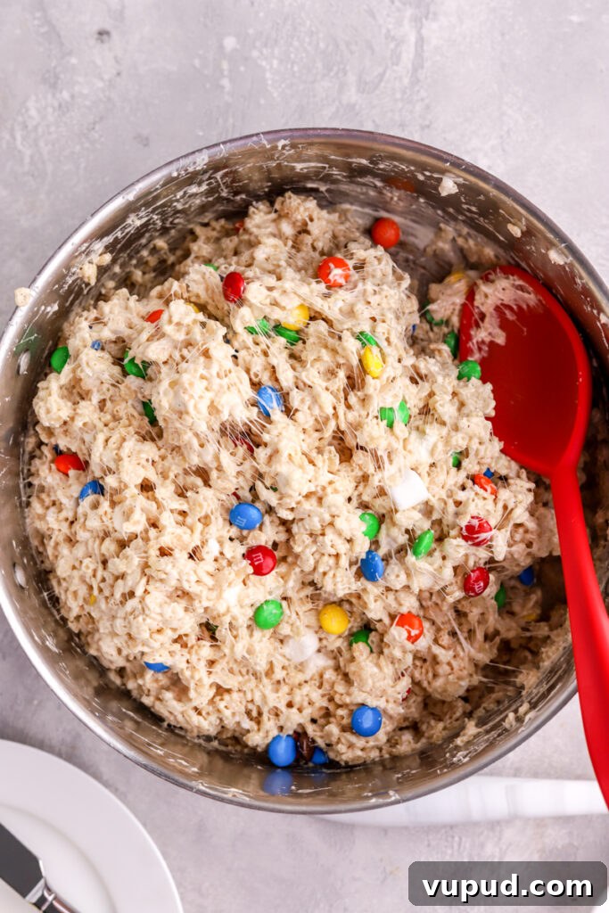 M&M Rice Krispie Treats Recipe: Colorful No-Bake Snack 10 M&M Rice Krispie Treats in a pot with a large red spoon in it.