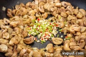 Indian Mushroom Bhaji Recipe: Flavorful Mushroom Curry Guide 8 Chopped mushrooms and fried chopped onions in a frying pan with chopped coriander stems, garlic and chilli