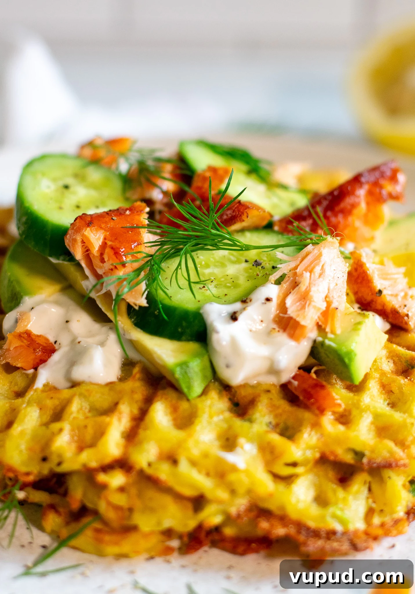 A stack of potato waffles topped with sour cream, smoked salmon, cucumber, and dill.