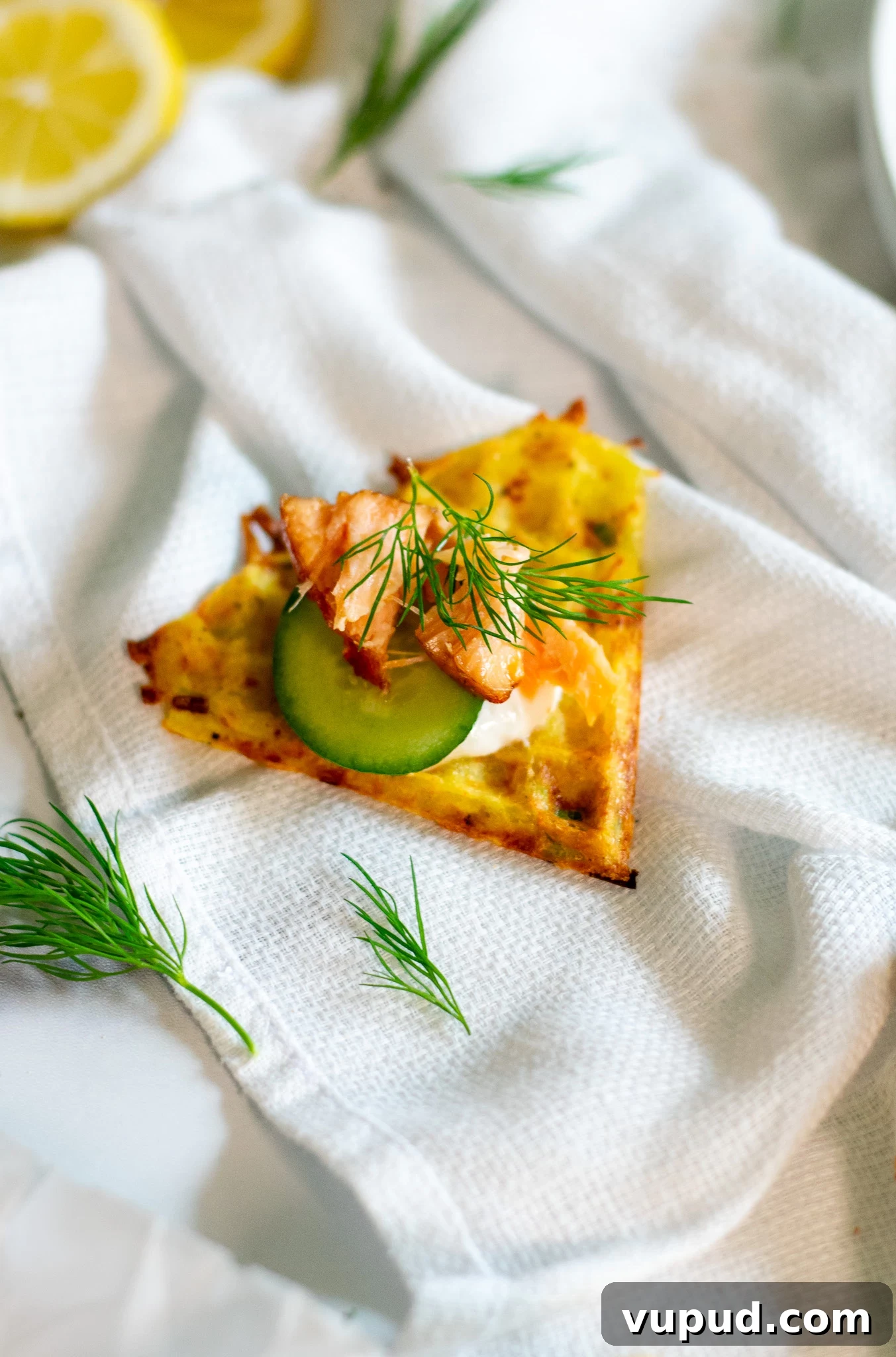 A slice of a potato waffle topped with smoked salmon, cucumber, and sour cream.