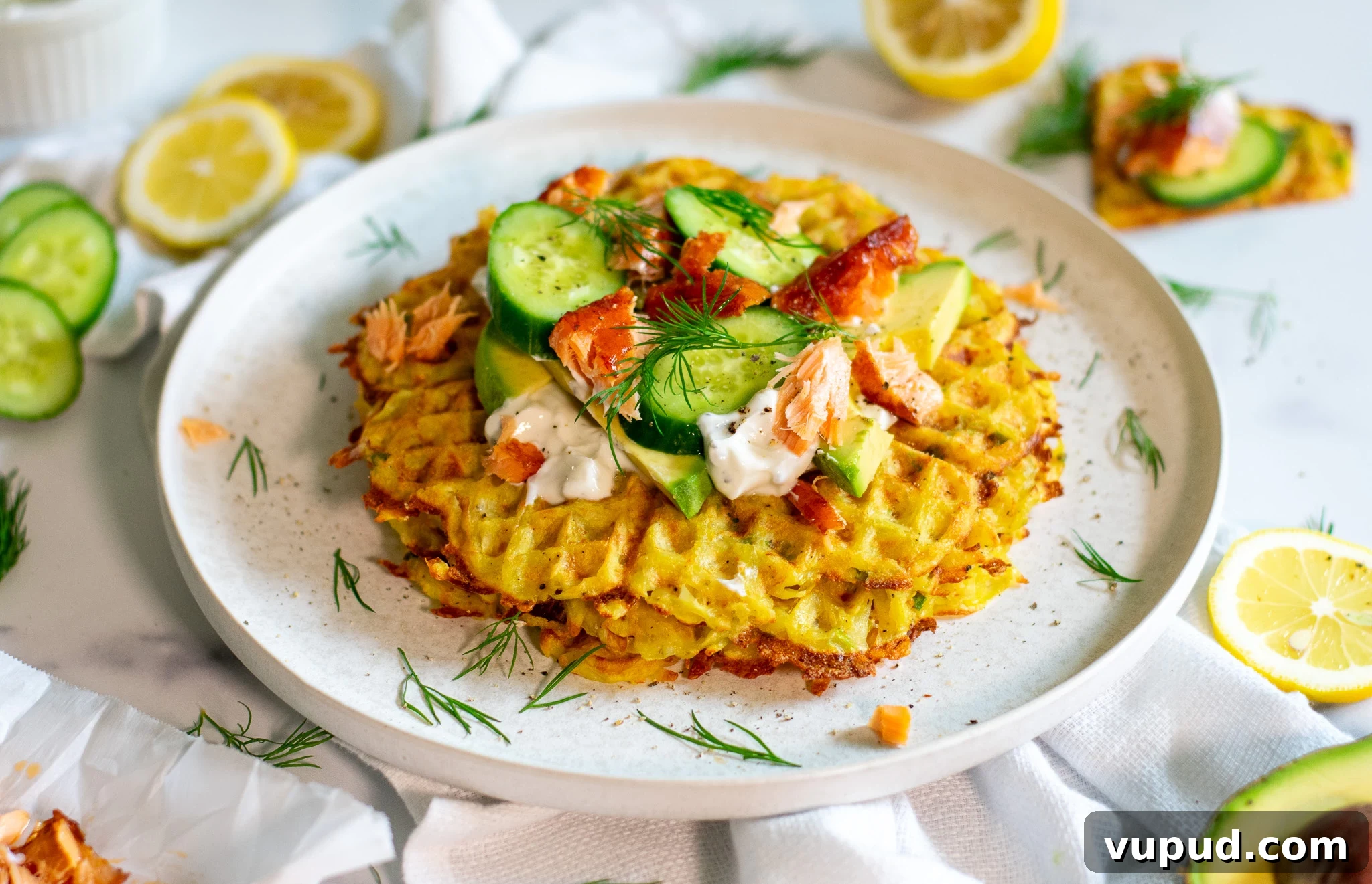 A stack of potato waffles topped with sour cream, smoked salmon, cucumber, and dill.