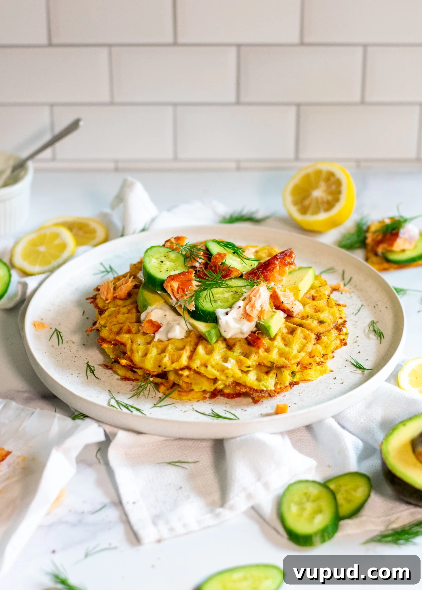 A stack of potato waffles topped with sour cream, smoked salmon, cucumber, and dill.