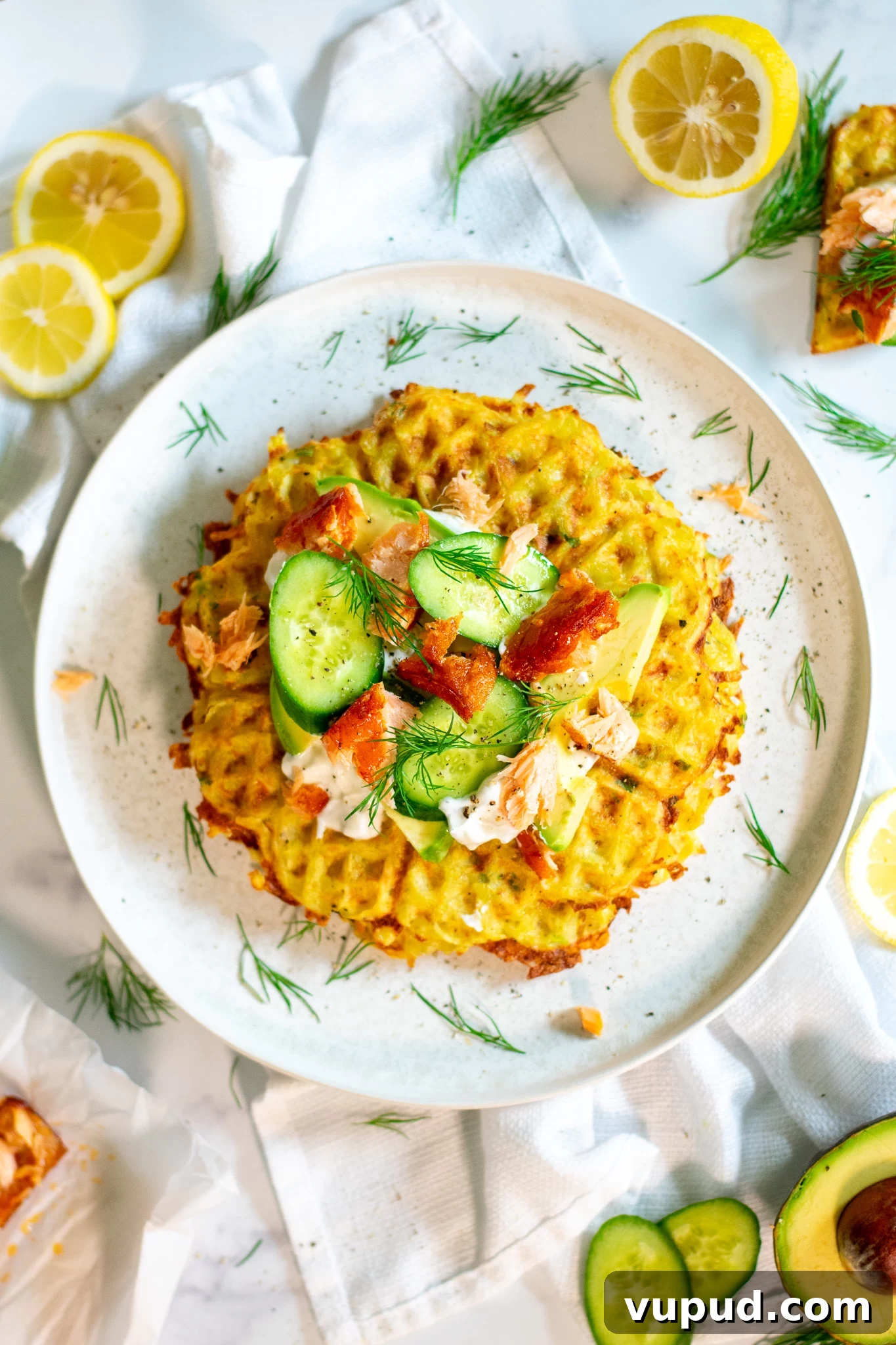 A stack of potato waffles topped with sour cream, smoked salmon, cucumber, and dill.