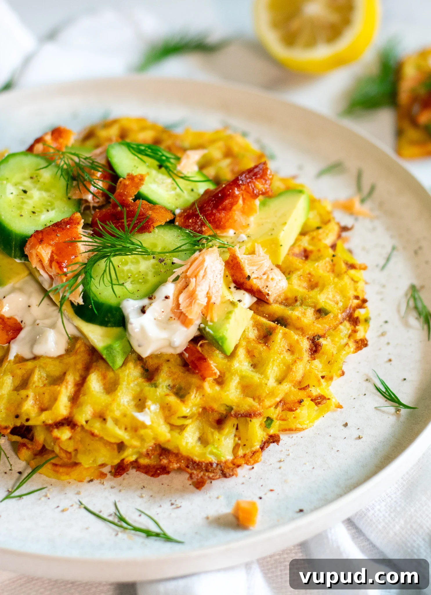 A stack of potato waffles topped with sour cream, smoked salmon, cucumber, and dill.