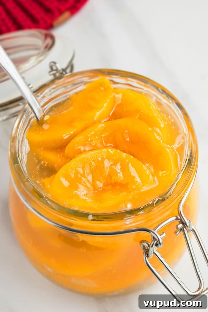 Easy Homemade Peach Pie Filling in Glass Jar on White Marble Background.
