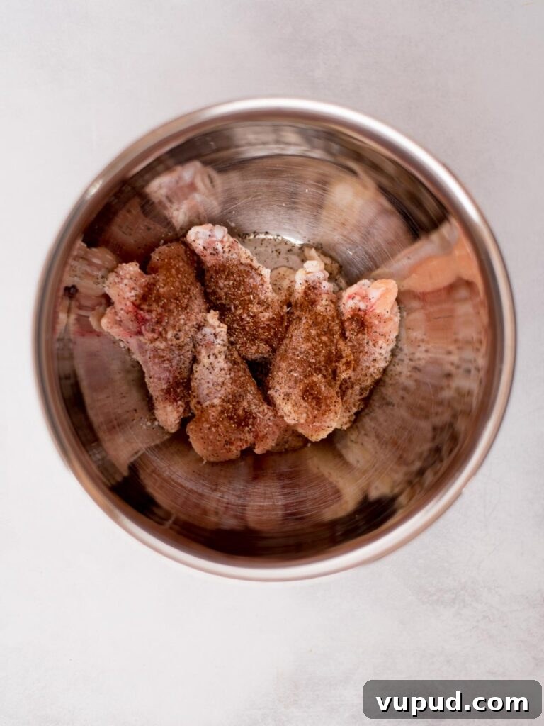 Tequila-Lime Chicken Wings: Zesty Grilled Wing Recipe 4 Raw chicken wings with seasonings added over them in a mixing bowl ready to combine.