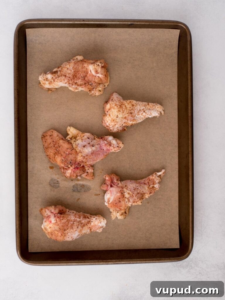 Tequila-Lime Chicken Wings: Zesty Grilled Wing Recipe 5 Seasoned raw chicken wings laying on parchment paper covered baking sheet.
