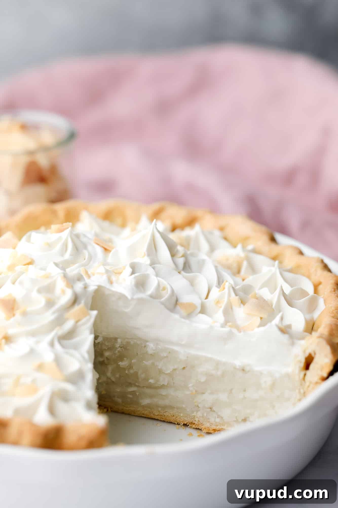 Creamy Vegan Coconut Cream Pie Recipe for Perfect Dessert 2 vegan coconut cream pie in a white pie plate with a slice removed.