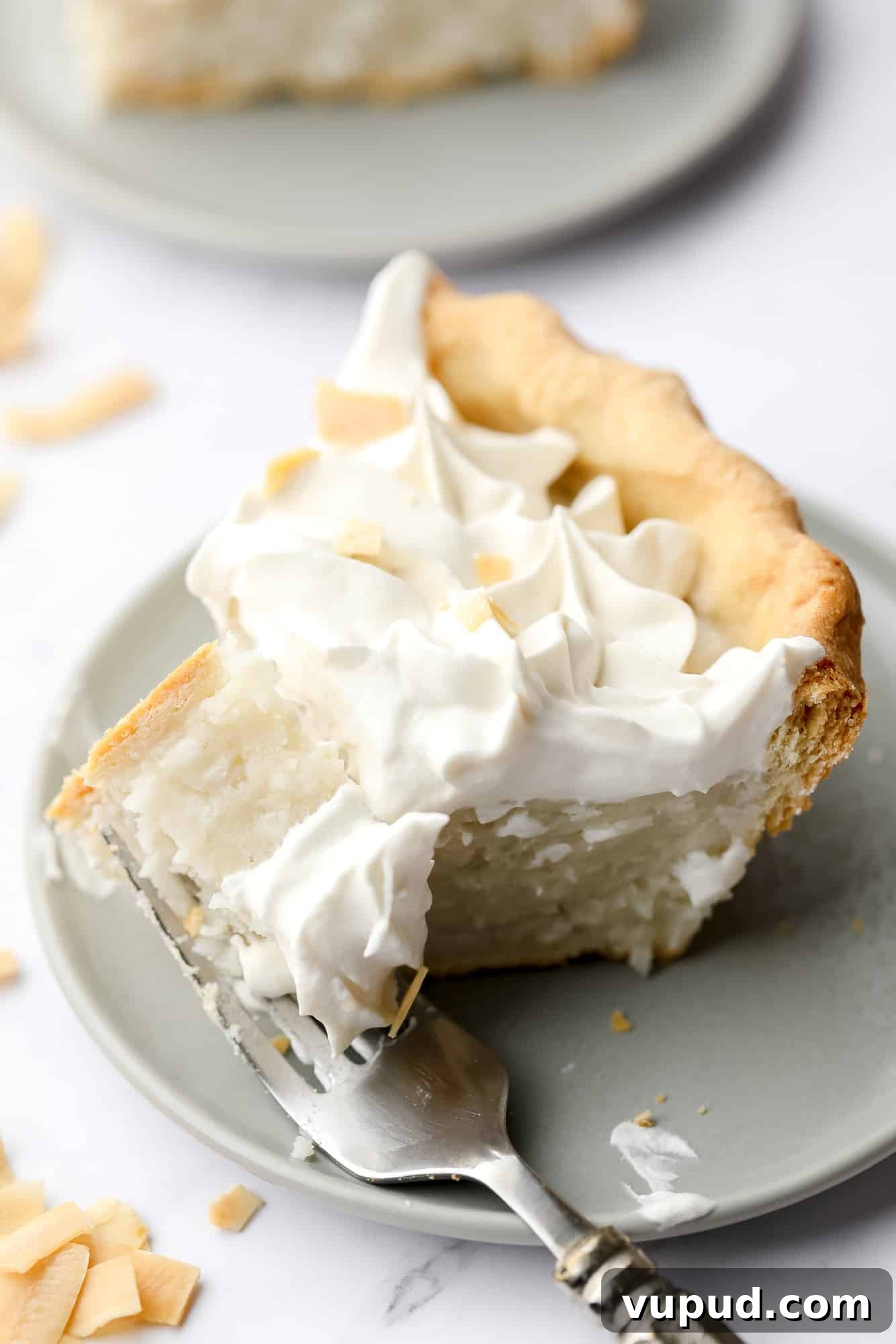 Creamy Vegan Coconut Cream Pie Recipe for Perfect Dessert 3 a fork taking a bite out of a slice of vegan coconut cream pie on a plate.