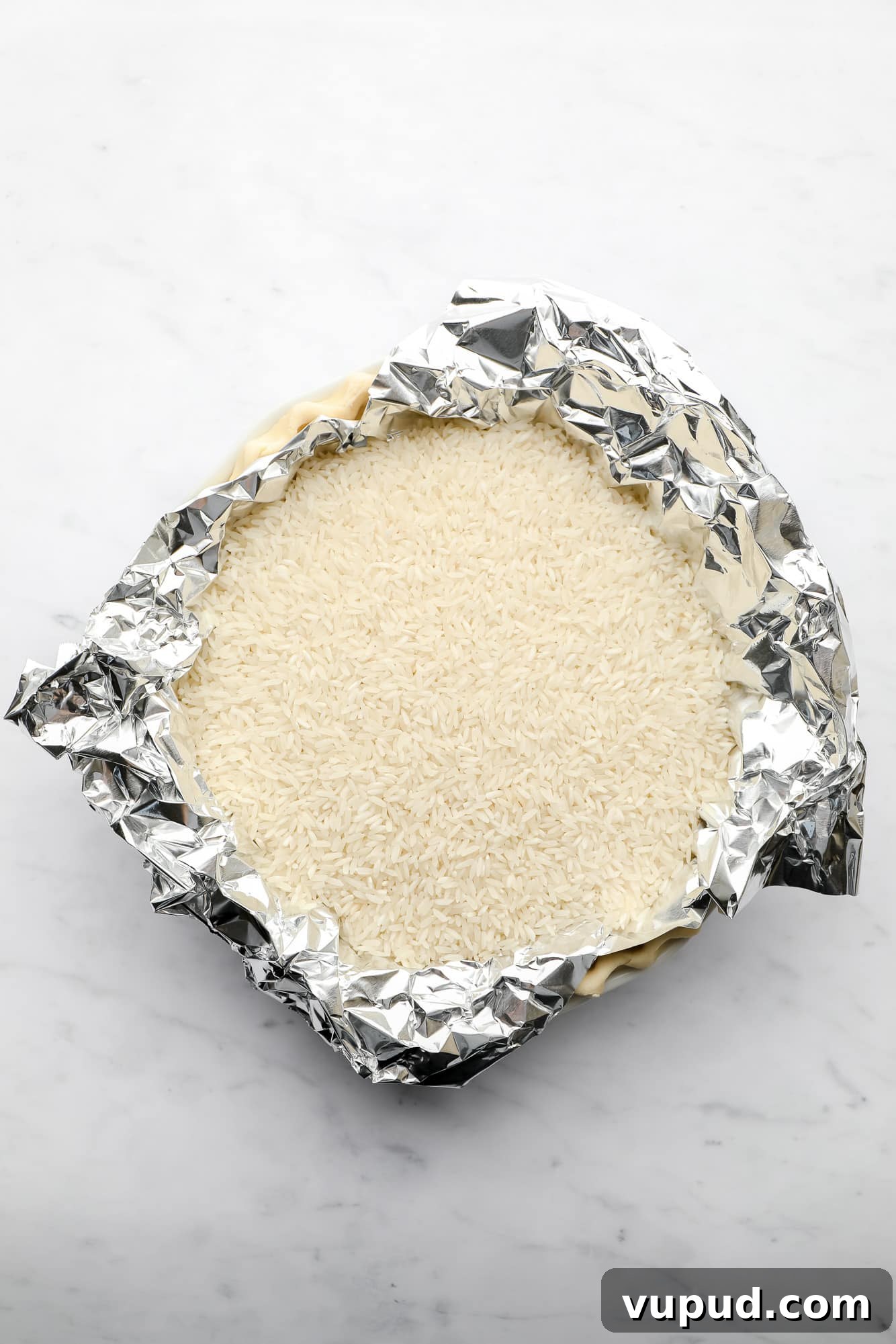 Creamy Vegan Coconut Cream Pie Recipe for Perfect Dessert 4 pie crust being baked in a pie plate with a layer of tinfoil and white rice on top.