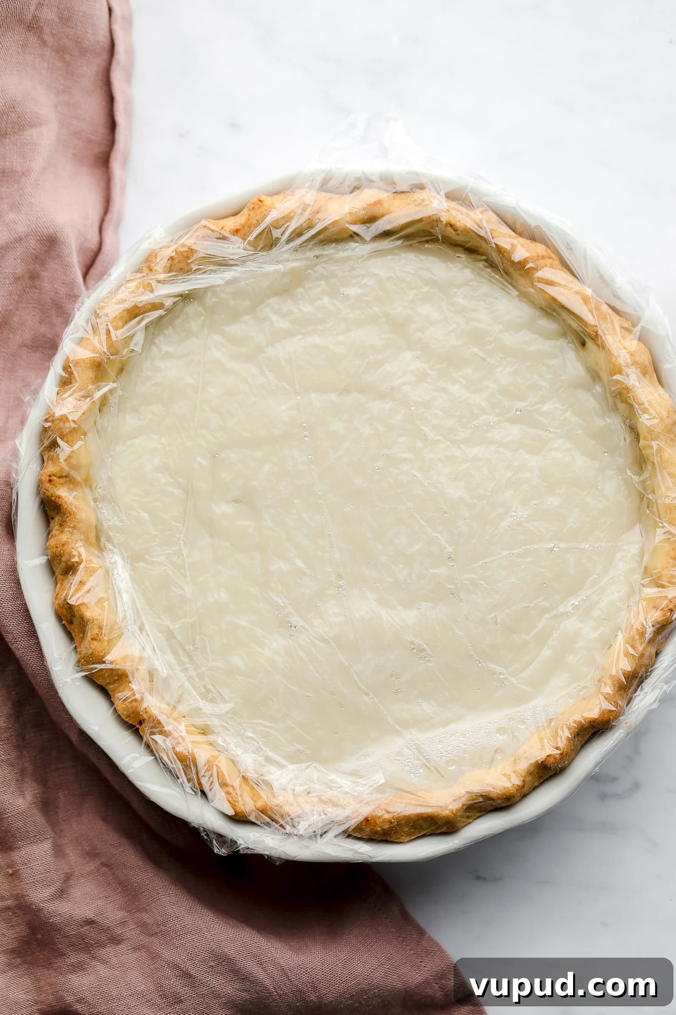 Creamy Vegan Coconut Cream Pie Recipe for Perfect Dessert 5 coconut custard in a pie covered with a layer of plastic wrap.