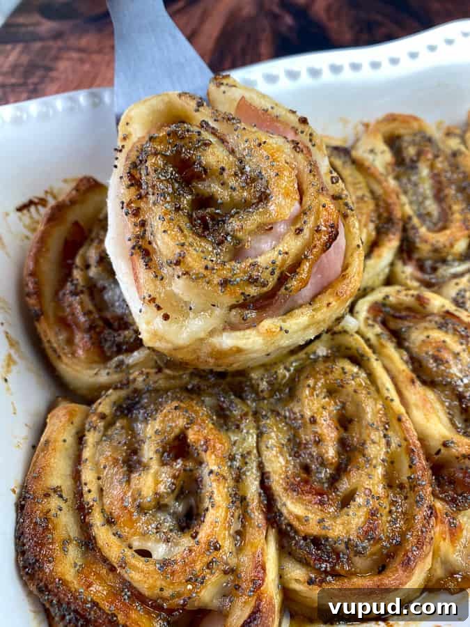 Quick Ham and Cheese Roll-Ups: 4-Ingredient Party Snack 3 Ham and cheese pinwheel on serving spatula above pan full of pinwheels