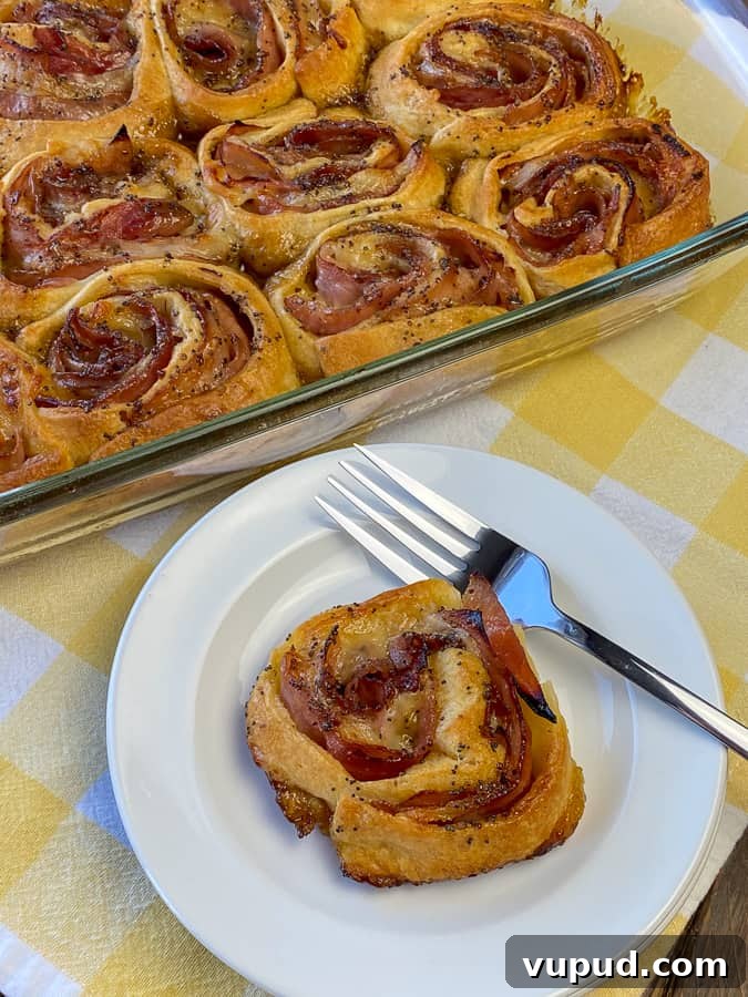 Quick Ham and Cheese Roll-Ups: 4-Ingredient Party Snack 4 Ham Roll-up on white plate with fork next to full baking dish on yellow plaid napkin