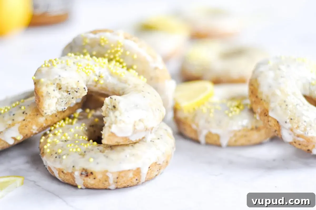 Gluten-Free Dairy-Free Lemon Donuts Recipe 2 A close-up of baked lemon poppy seed donuts with yellow sprinkles and one donut has a bite taken out of it.