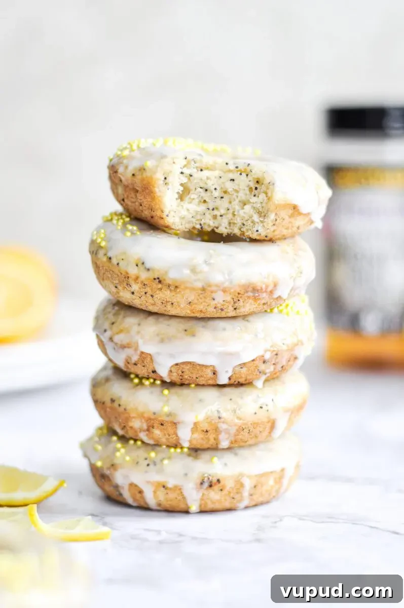 Gluten-Free Dairy-Free Lemon Donuts Recipe 3 A stack of baked lemon poppy seed donuts with a white glaze and yellow sprinkles on top.