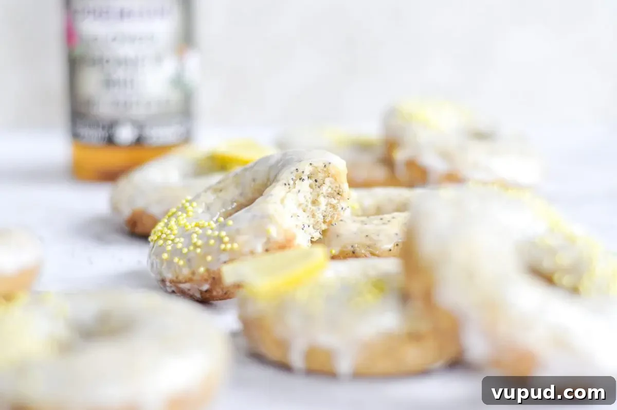 Gluten-Free Dairy-Free Lemon Donuts Recipe 4 A close-up shot of a lemon poppy seed donut with a white glaze on top, yellow sprinkles, and a bite taken out of it.