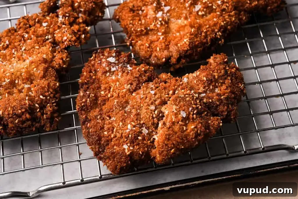 what is Chicken schnitzel Crispy, golden brown chicken schnitzel resting on a wire rack after frying, topped with sesame seeds and flaky salt.