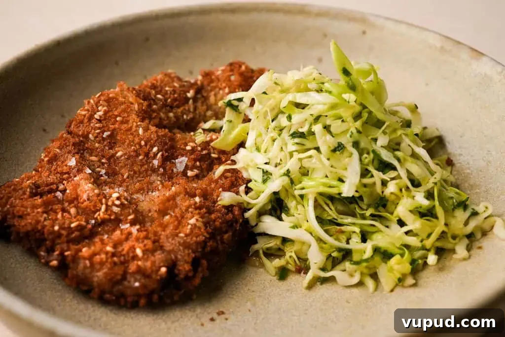 chicken schnitzel A plate featuring golden-brown chicken schnitzel next to a fresh cabbage slaw.