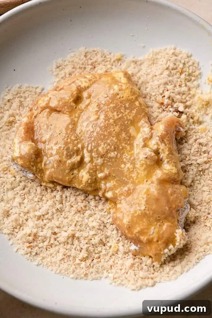 how to make Chicken schnitzel Chicken coated in an egg mixture being pressed into a plate of panko breadcrumbs.