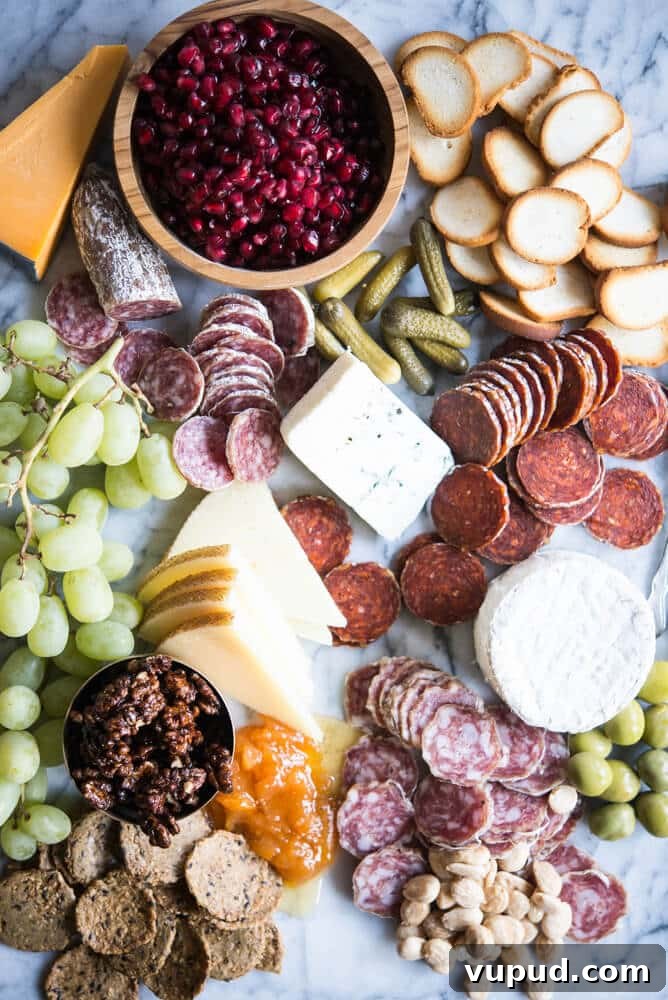 Perfect Charcuterie Board Guide: Build an Elegant Spread for Any Occasion 2 Charcuterie board with meats, cheeses, honey, nuts, a wooden bowl of pomegranates, olives, grapes, pickles, crackers, on a marble board