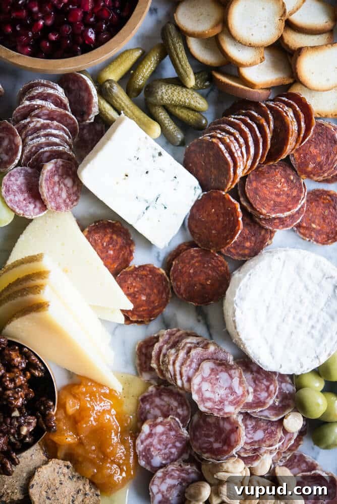 Perfect Charcuterie Board Guide: Build an Elegant Spread for Any Occasion 3 Charcuterie board with meats, cheeses, honey, nuts, a wooden bowl of pomegranates, olives, grapes, pickles, crackers, on a marble board