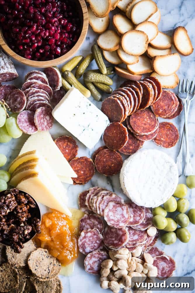 Perfect Charcuterie Board Guide: Build an Elegant Spread for Any Occasion 4 Charcuterie board with meats, cheeses, honey, nuts, a wooden bowl of pomegranates, olives, grapes, pickles, crackers, on a marble board