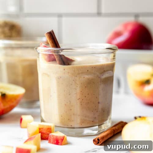 A small glass filled with apple banana smoothie and garnished with a cinnamon stick.